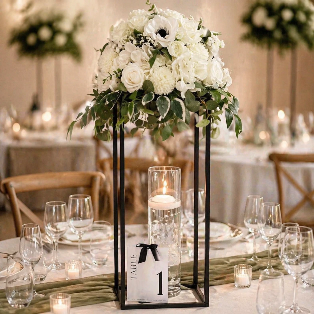 Close-up of tall black geometric centrepiece stand with white floral topper and hurricane candle vase